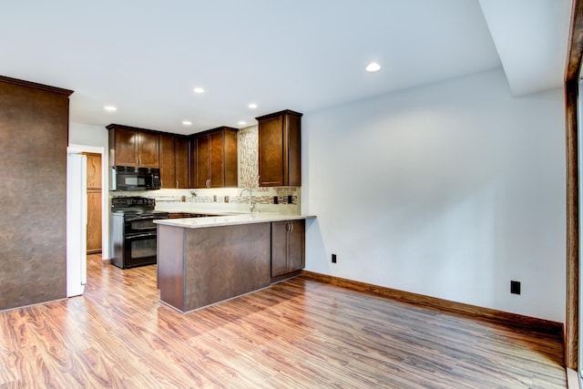 kitchen with sink, kitchen peninsula, black appliances, light hardwood / wood-style floors, and decorative backsplash