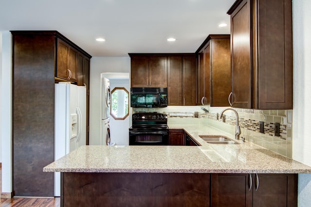 kitchen featuring sink, dark wood-type flooring, black appliances, light stone countertops, and stacked washer / drying machine