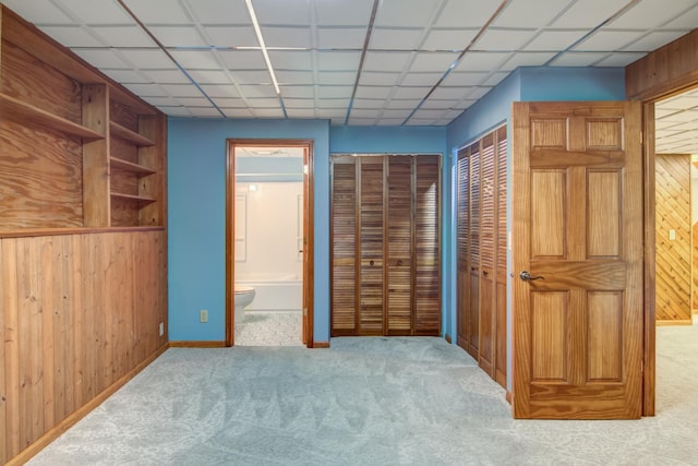 unfurnished bedroom featuring connected bathroom, wooden walls, two closets, and light carpet