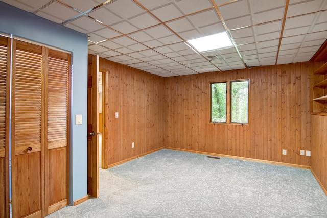 interior space featuring light colored carpet, wooden walls, and a paneled ceiling