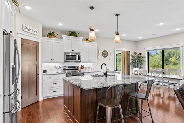 kitchen featuring a sink, backsplash, appliances with stainless steel finishes, a kitchen breakfast bar, and dark wood-style flooring