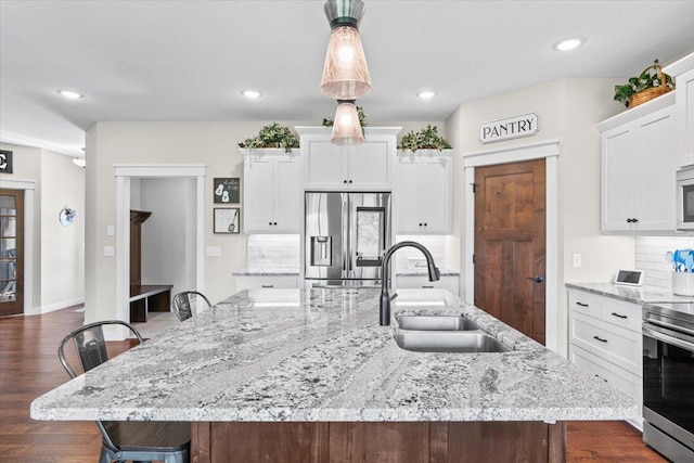 kitchen featuring a large island with sink, a sink, stainless steel appliances, white cabinetry, and a kitchen breakfast bar