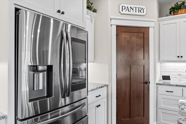 kitchen with decorative backsplash, white cabinetry, stainless steel refrigerator with ice dispenser, and light stone countertops