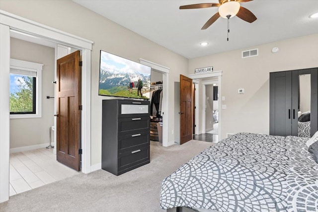 bedroom featuring light carpet, visible vents, a walk in closet, and baseboards