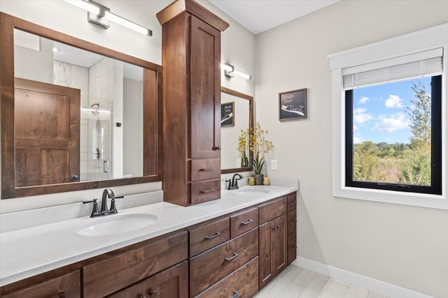 full bath with a shower stall, double vanity, baseboards, and a sink