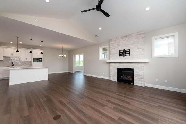 unfurnished living room with ceiling fan with notable chandelier, a fireplace, dark hardwood / wood-style flooring, and lofted ceiling