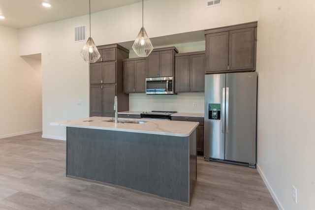 kitchen featuring hanging light fixtures, light hardwood / wood-style flooring, stainless steel appliances, sink, and a center island with sink