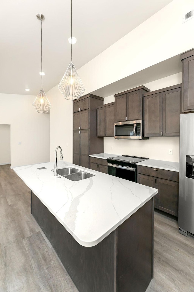 kitchen with hanging light fixtures, light wood-type flooring, appliances with stainless steel finishes, sink, and a kitchen island with sink