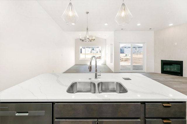 kitchen with a large fireplace, light stone counters, open floor plan, wood finished floors, and a sink