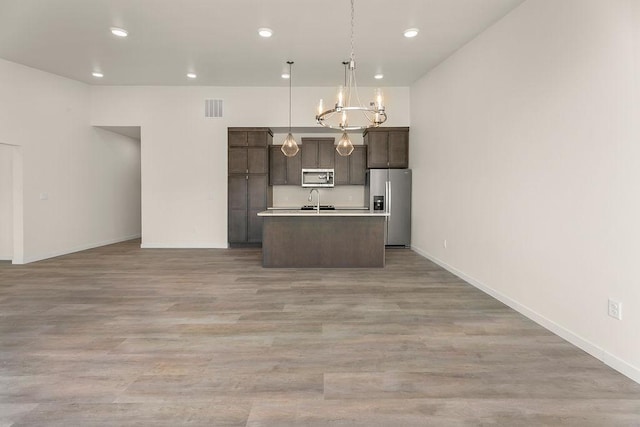 kitchen featuring decorative light fixtures, stainless steel appliances, light hardwood / wood-style floors, and a kitchen island with sink