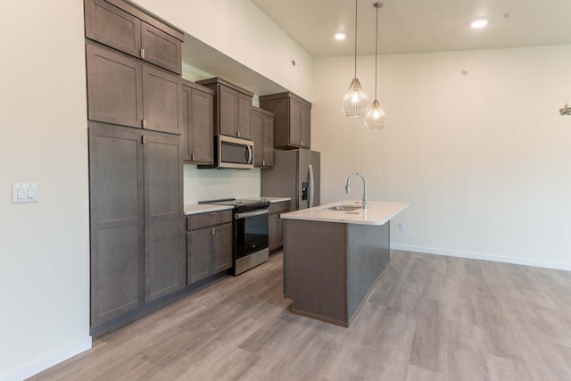 kitchen with a kitchen island with sink, stainless steel appliances, a sink, baseboards, and light wood-style floors