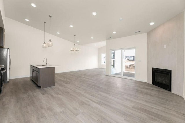 unfurnished living room featuring a large fireplace, sink, wood-type flooring, and an inviting chandelier