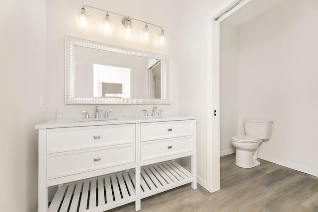 full bathroom with toilet, wood finished floors, a sink, baseboards, and double vanity