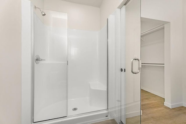 bathroom featuring a stall shower, a spacious closet, baseboards, and wood finished floors