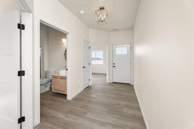 corridor featuring light wood-style floors, visible vents, baseboards, and a notable chandelier