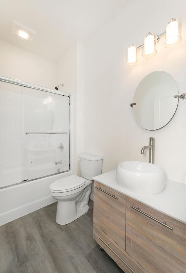 full bathroom featuring vanity, bath / shower combo with glass door, wood finished floors, and toilet