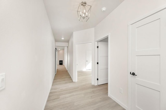 corridor featuring light wood-style floors, baseboards, and an inviting chandelier