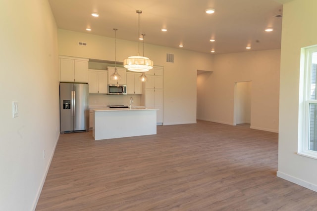 kitchen featuring light wood-type flooring, pendant lighting, appliances with stainless steel finishes, a center island with sink, and white cabinets