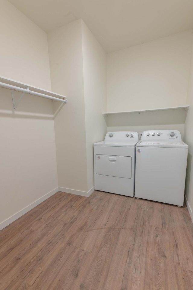 clothes washing area with washing machine and clothes dryer and light hardwood / wood-style floors