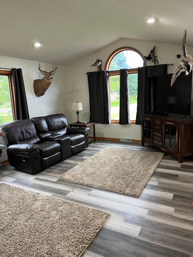 living area with vaulted ceiling, wood finished floors, visible vents, and a wealth of natural light