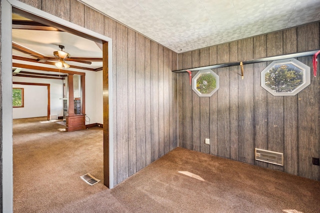 empty room featuring wood walls, carpet, visible vents, and ceiling fan