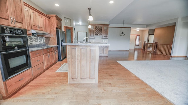 kitchen featuring black appliances, light hardwood / wood-style floors, and an island with sink