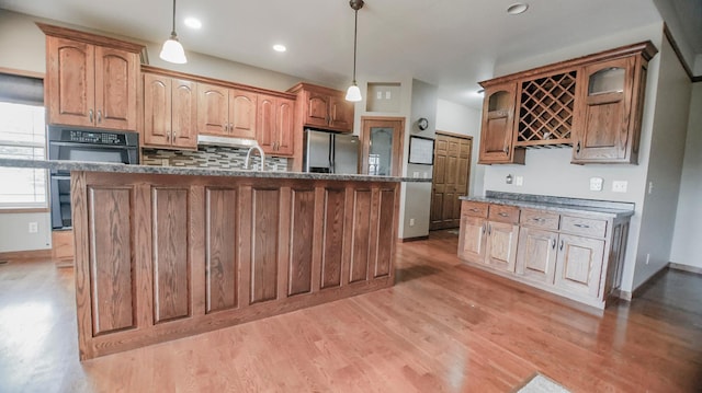 kitchen with stainless steel refrigerator with ice dispenser, decorative light fixtures, light wood-type flooring, and a kitchen island with sink