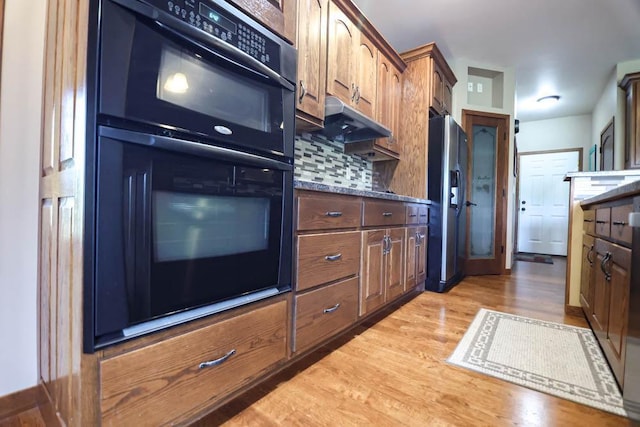 kitchen with black appliances, decorative backsplash, light hardwood / wood-style floors, and dark stone counters