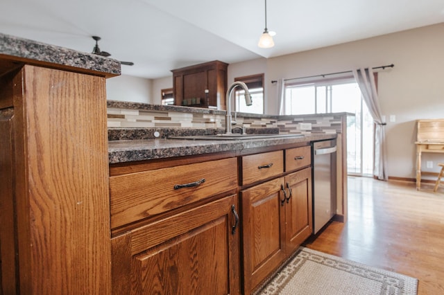 kitchen featuring backsplash, dishwasher, light hardwood / wood-style floors, sink, and pendant lighting