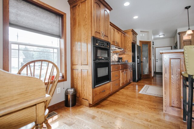 kitchen with decorative backsplash, pendant lighting, black appliances, and light hardwood / wood-style floors