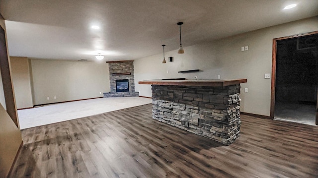 unfurnished living room with indoor bar, a stone fireplace, and dark hardwood / wood-style flooring