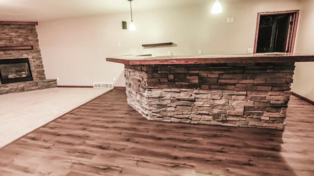 bar featuring dark wood-type flooring, hanging light fixtures, and a stone fireplace