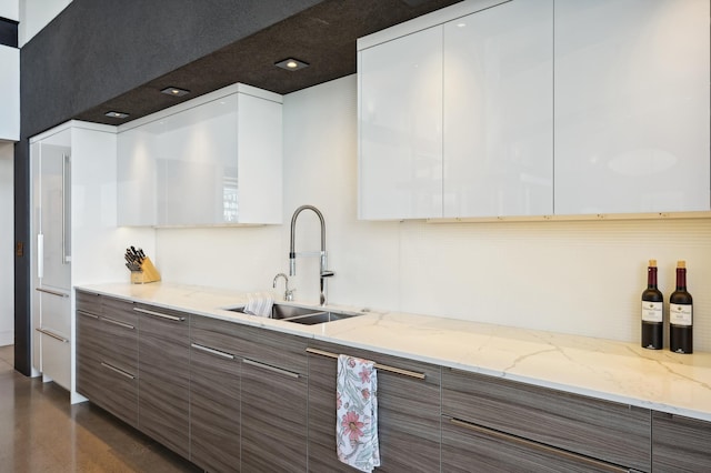 kitchen with dark brown cabinets, white cabinets, light stone counters, and sink