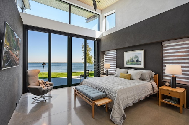 bedroom featuring a high ceiling, a water view, access to exterior, and concrete floors