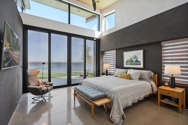 bedroom with multiple windows, a high ceiling, a water view, and concrete floors