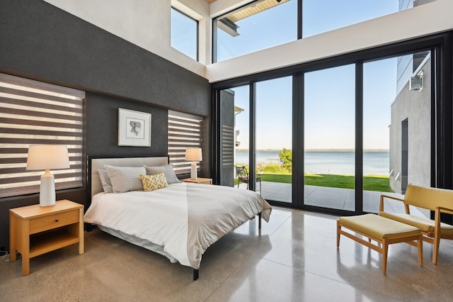 bedroom featuring concrete flooring, a water view, a towering ceiling, and access to exterior