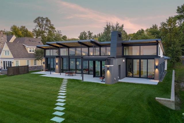 back house at dusk featuring a patio, a yard, and a sunroom