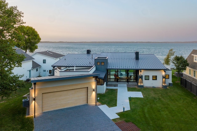 view of front of home featuring a water view, cooling unit, a lawn, and a garage