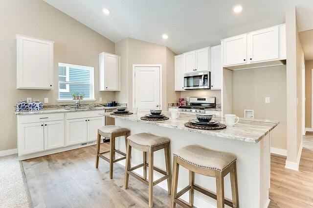 kitchen with white cabinets, a kitchen island, stainless steel appliances, and vaulted ceiling