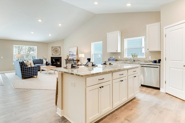 kitchen featuring light wood-type flooring, light stone countertops, white cabinetry, a kitchen island, and stainless steel dishwasher