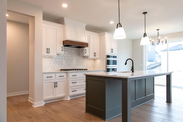 kitchen with a center island with sink, light wood-type flooring, custom exhaust hood, gas cooktop, and a sink