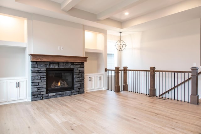 unfurnished living room featuring beam ceiling, a notable chandelier, built in shelves, light wood-style floors, and a stone fireplace