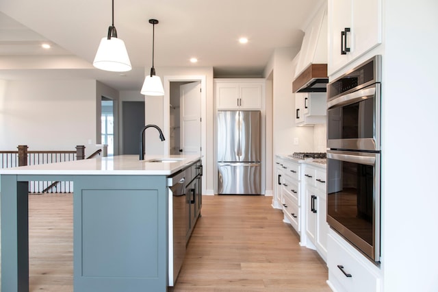 kitchen featuring premium range hood, a center island with sink, light countertops, stainless steel appliances, and a sink