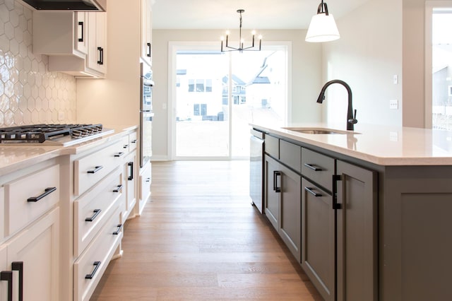 kitchen featuring gray cabinetry, light wood-style flooring, a sink, stainless steel appliances, and decorative backsplash