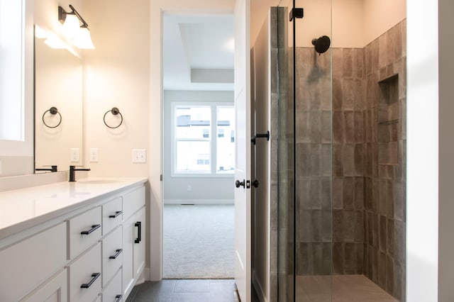 bathroom featuring tile patterned flooring, tiled shower, vanity, and baseboards