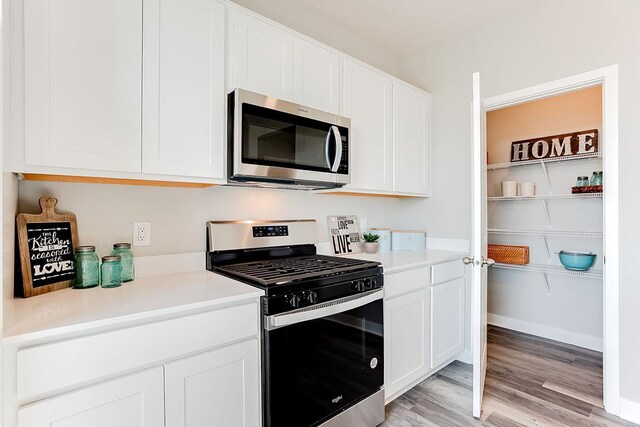 kitchen with stainless steel appliances, light wood-type flooring, light countertops, and white cabinetry