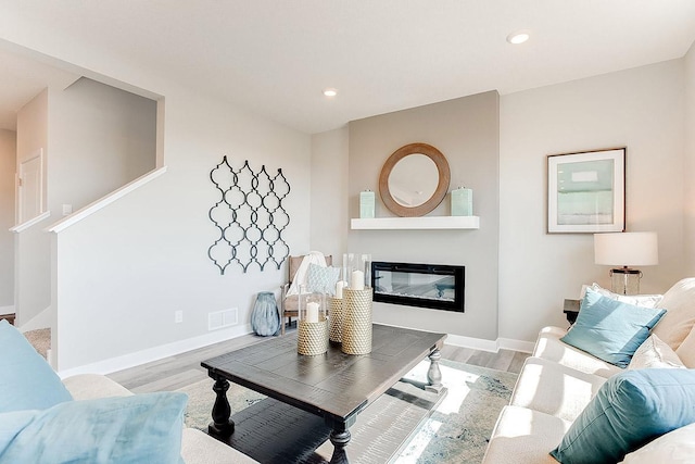 living room featuring baseboards, wood finished floors, and a glass covered fireplace