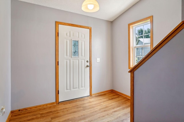 entrance foyer featuring lofted ceiling, light wood-type flooring, and a textured ceiling