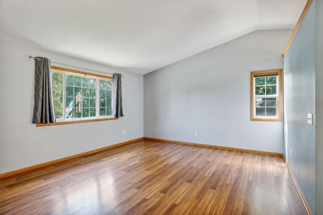 empty room with vaulted ceiling, a textured ceiling, and hardwood / wood-style flooring