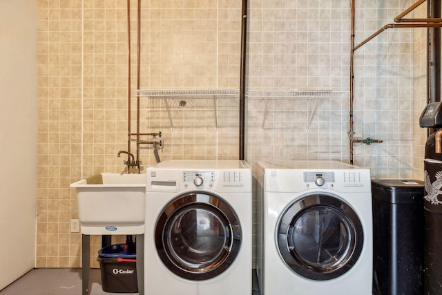 clothes washing area with tile walls, washer and dryer, and sink